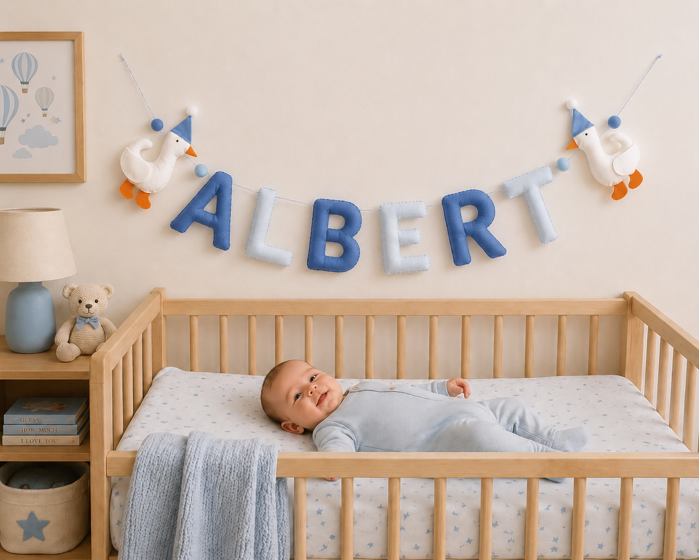 Baby lying in a crib with 'ALBERT' name garland spelled out on the wall above.