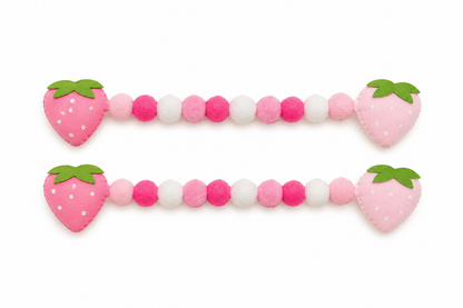 Pink and white beaded toy with strawberry-shaped ends on a white background