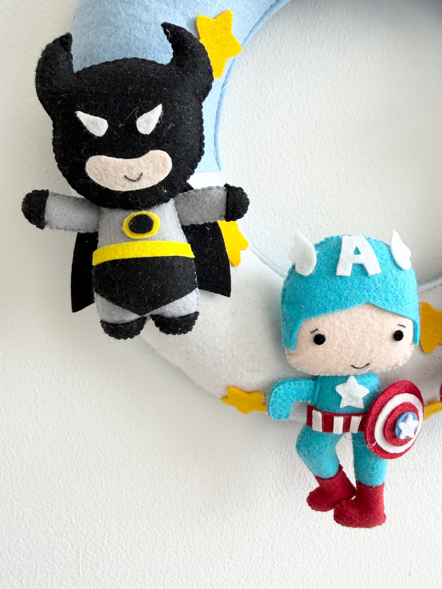 Two superhero felt toys, one resembling Batman and the other resembling Captain America, on a white background.