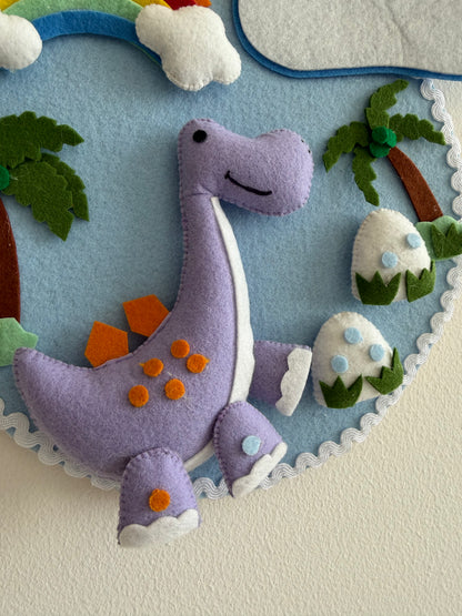 Felt dinosaur toy with a colorful background featuring trees and eggs.